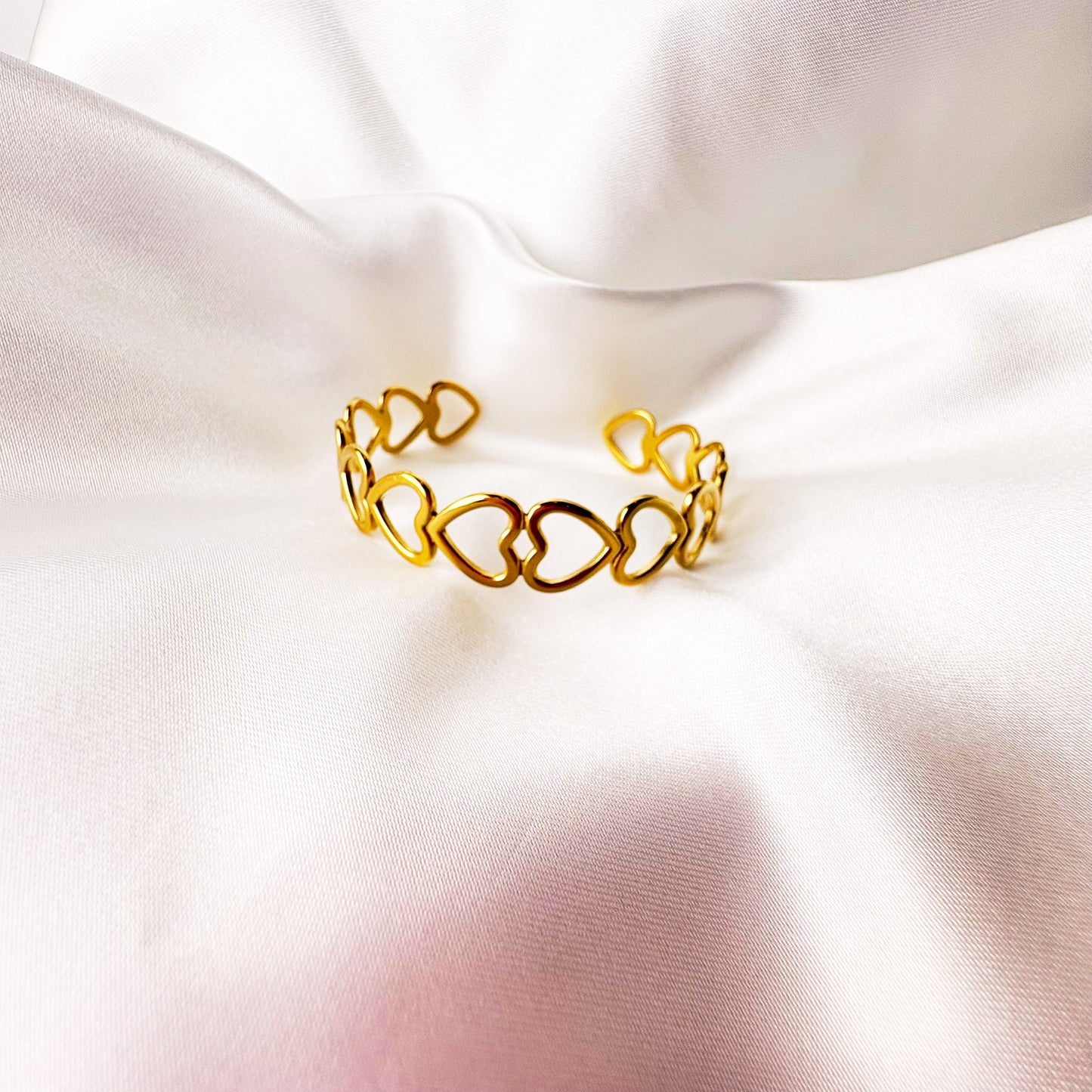 Gold heart-shaped bracelet on a soft white fabric background