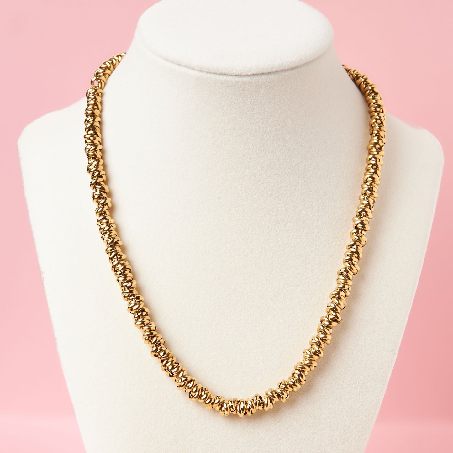 Gold necklace on a white mannequin bust against a pink background