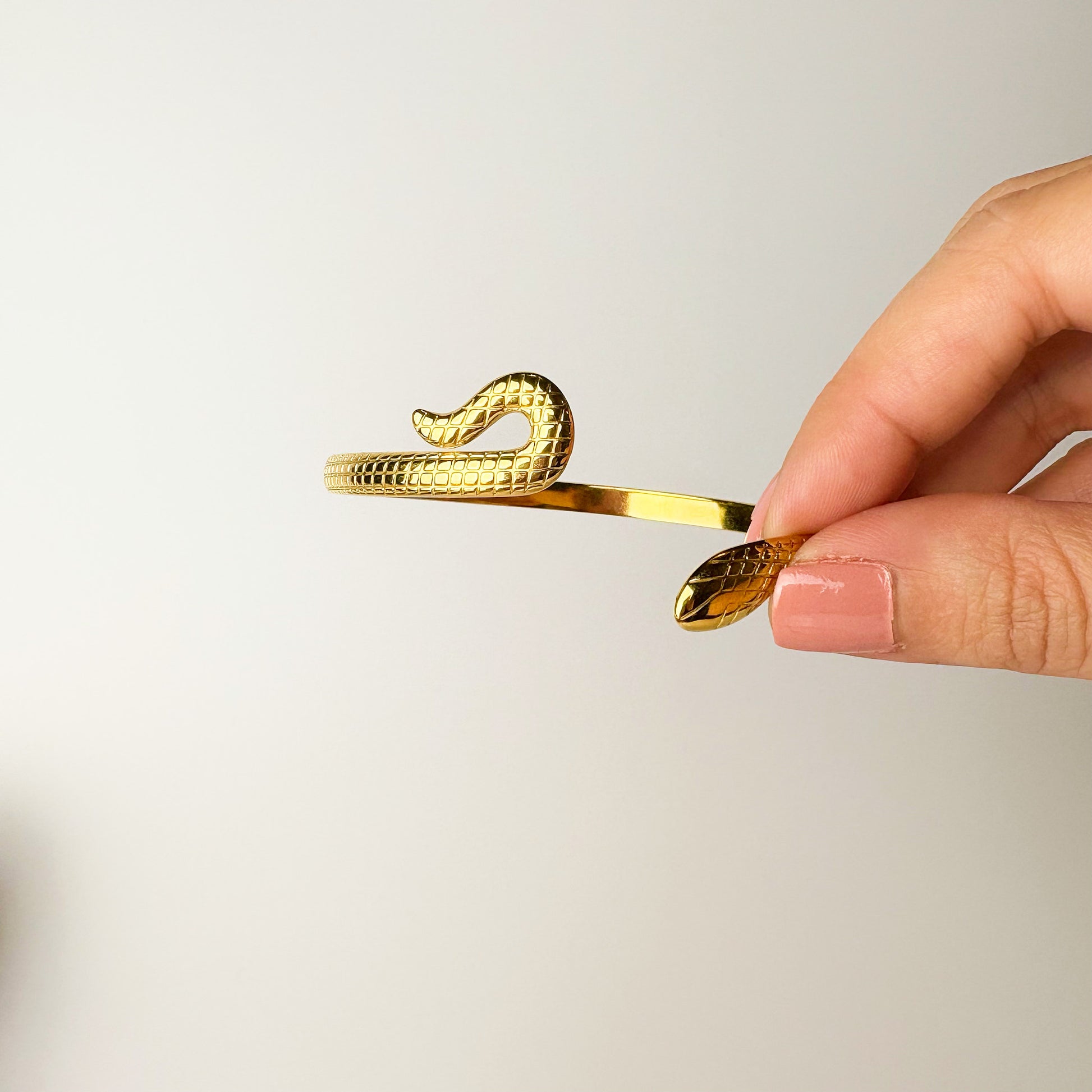 Gold snake-shaped hair clip held by a hand against a light background