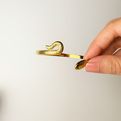 Gold snake-shaped hair clip held by a hand against a light background