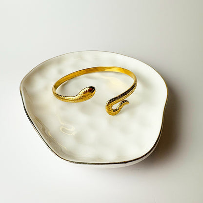Gold snake-shaped bracelet on a white dish with a neutral background