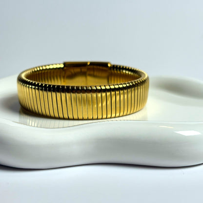Gold bracelet on a white ceramic dish with a light gray background
