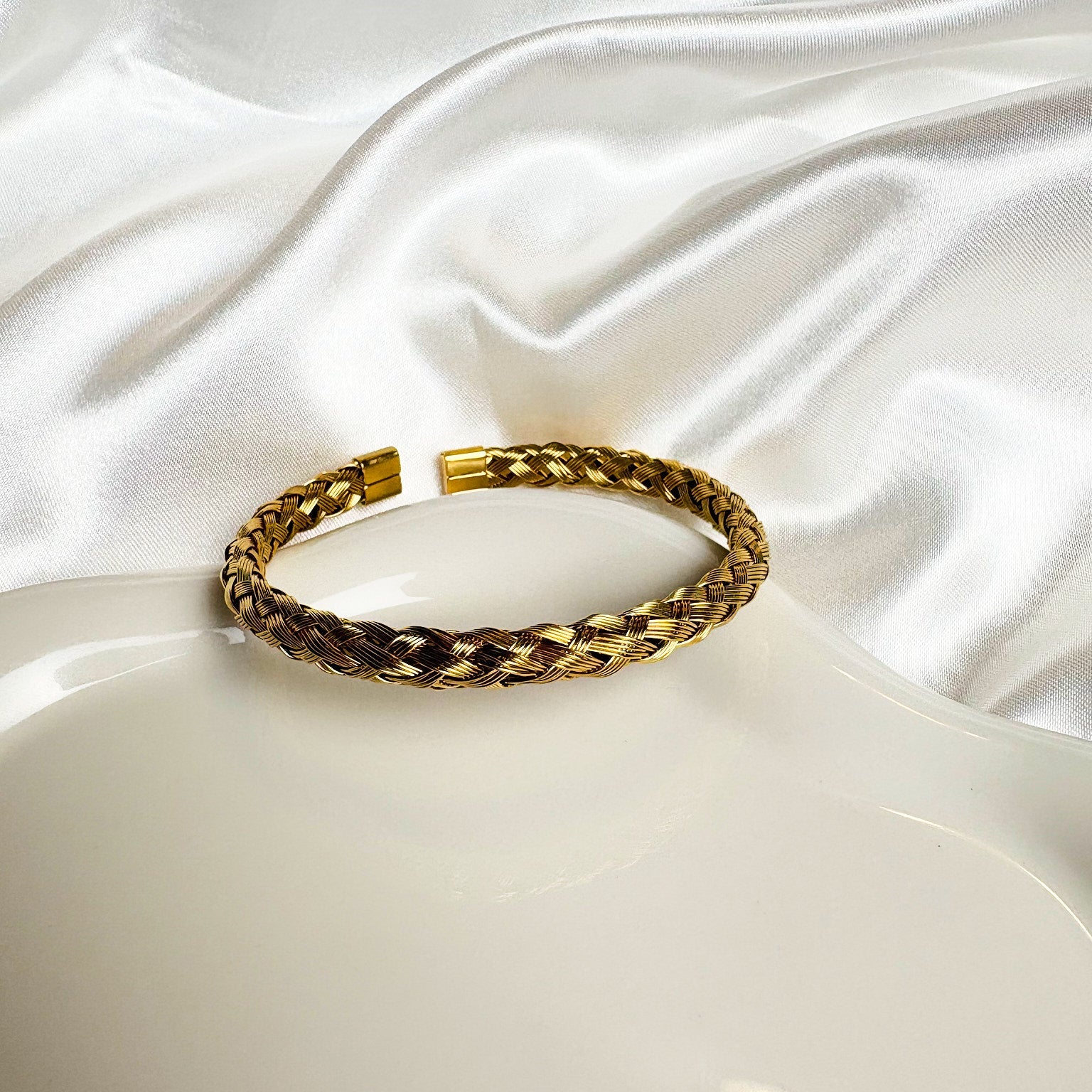 Gold braided bracelet on a white satin surface