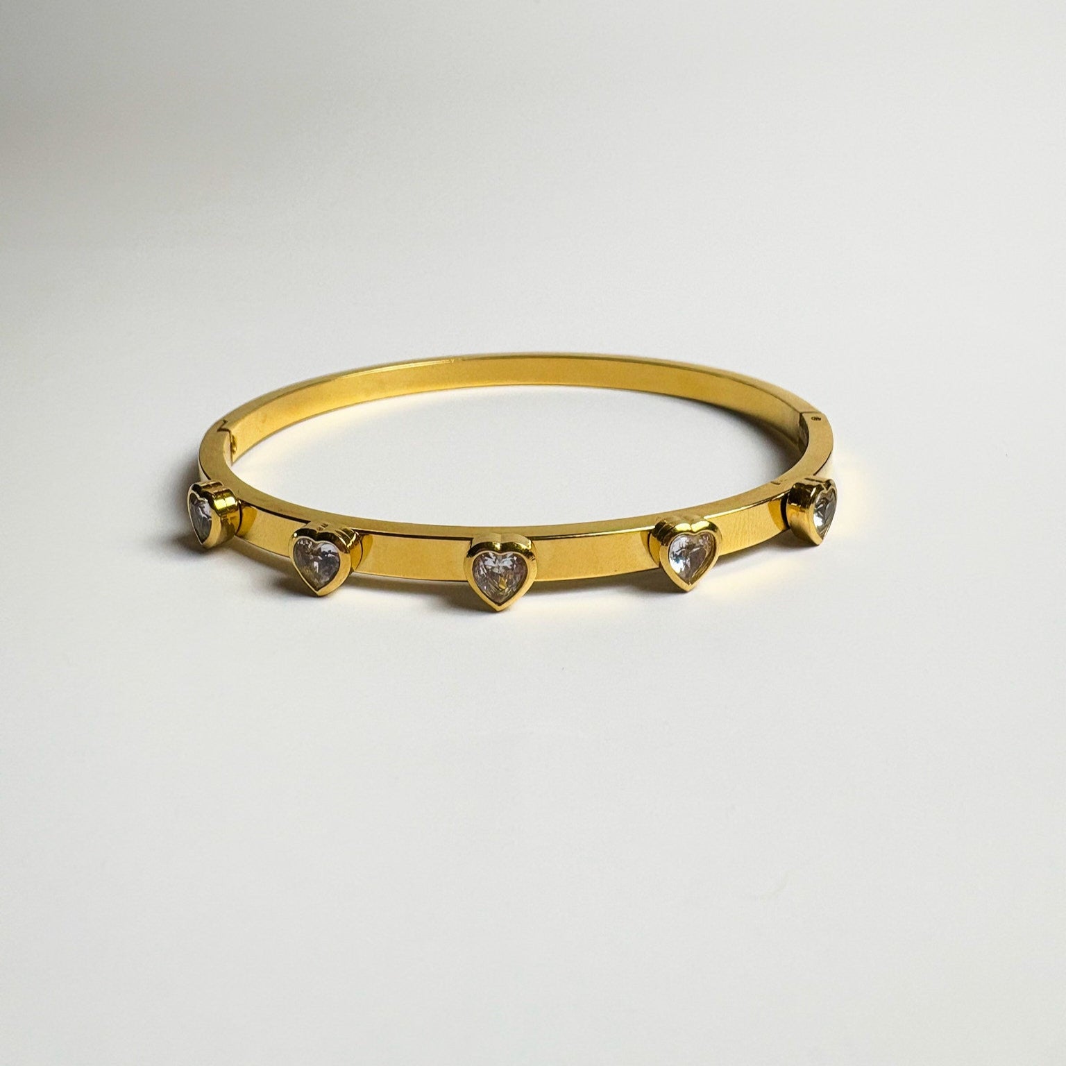 Gold bracelet with heart-shaped stones on a light gray background