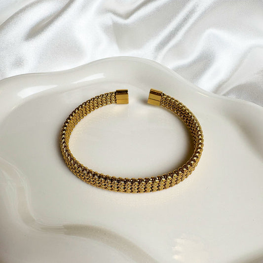 Gold bracelet on a white, textured surface