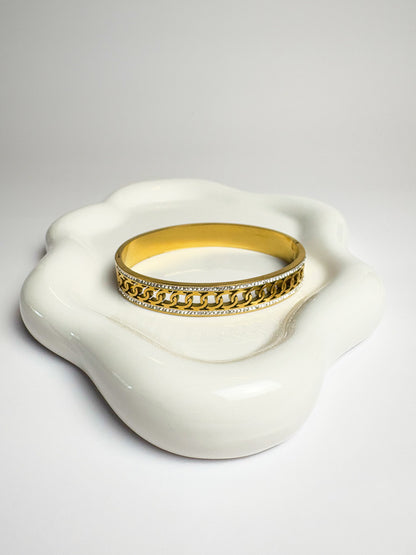 Gold bracelet with chain design on a white ceramic dish