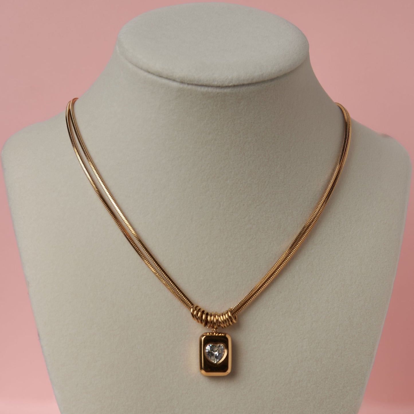 Gold necklace with a pendant on a mannequin bust against a pink background