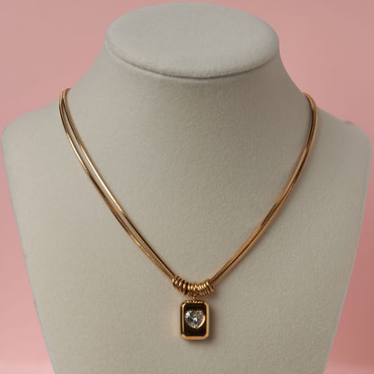 Gold necklace with a pendant on a mannequin bust against a pink background